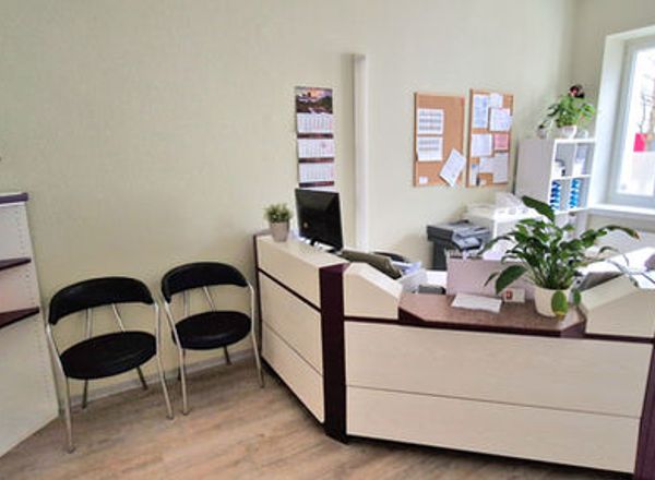 Moderner Empfangsbereich einer Arztpraxis mit hellem Tresen, schwarzen Besucherstühlen und grünen Pflanzen